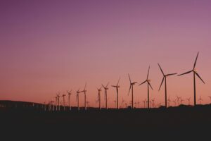 Row of wind turbines generating renewable energy at sunset with a purple and orange sky in the background.